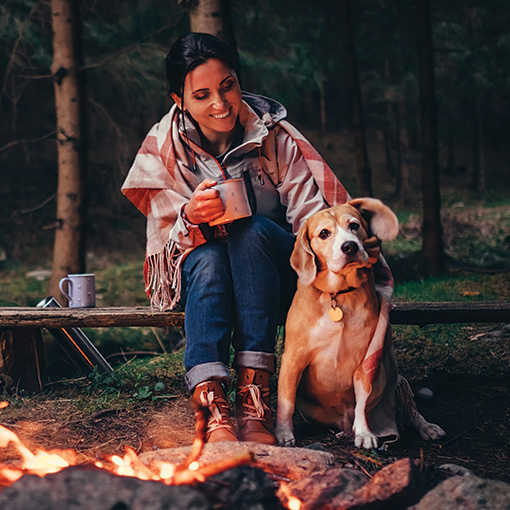 woman and dog sitting at campfire